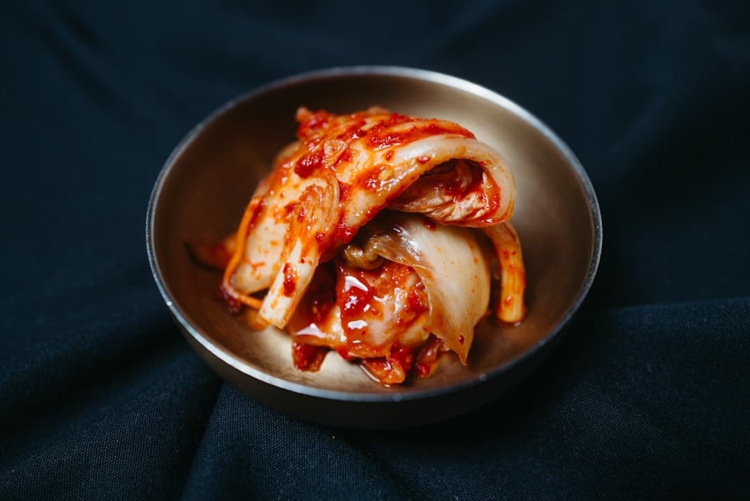 Red kimchi in a brass bowl on navy fabric.