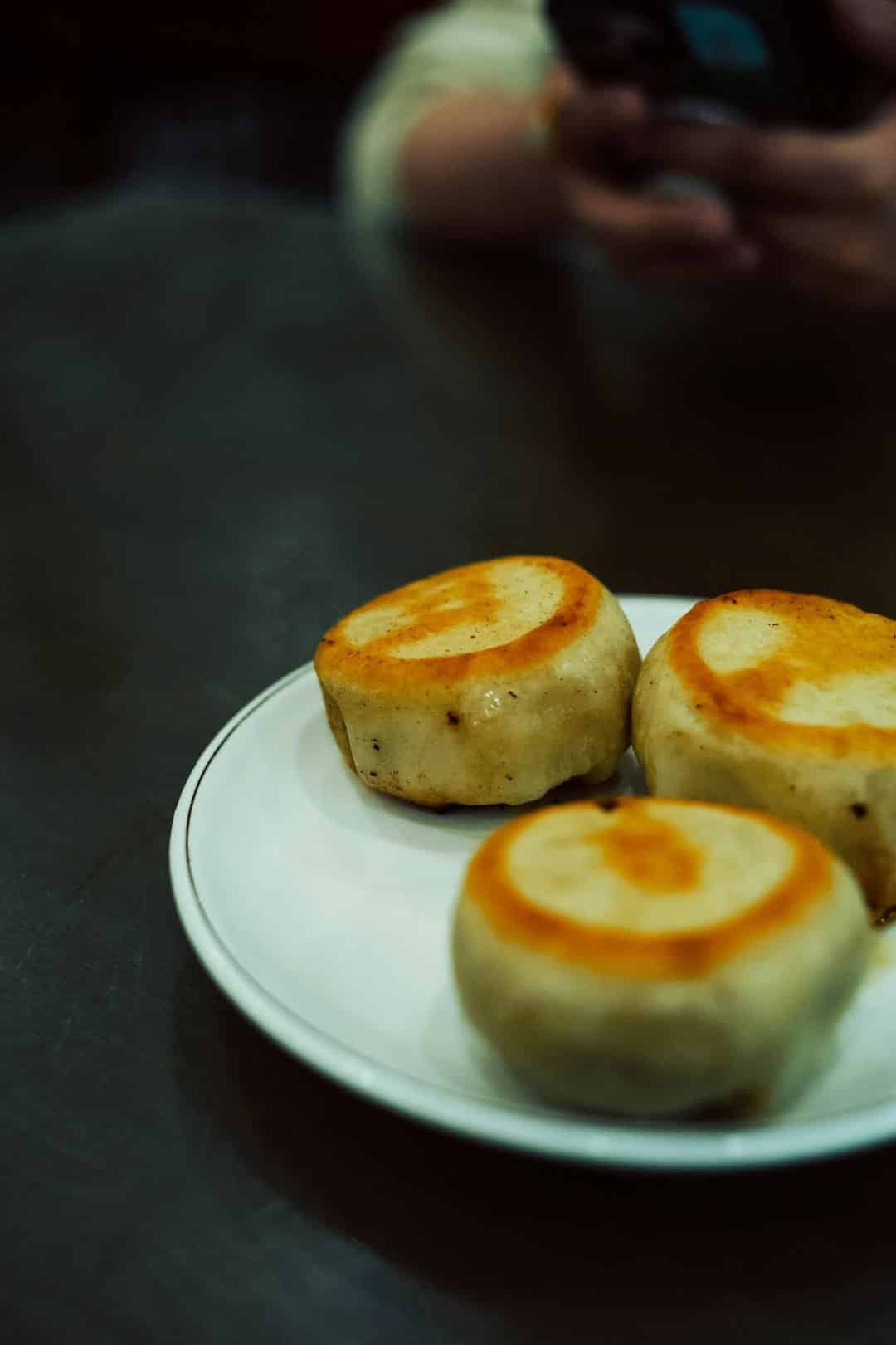 Three golden-brown pan-fried dumplings arranged on a white plate.