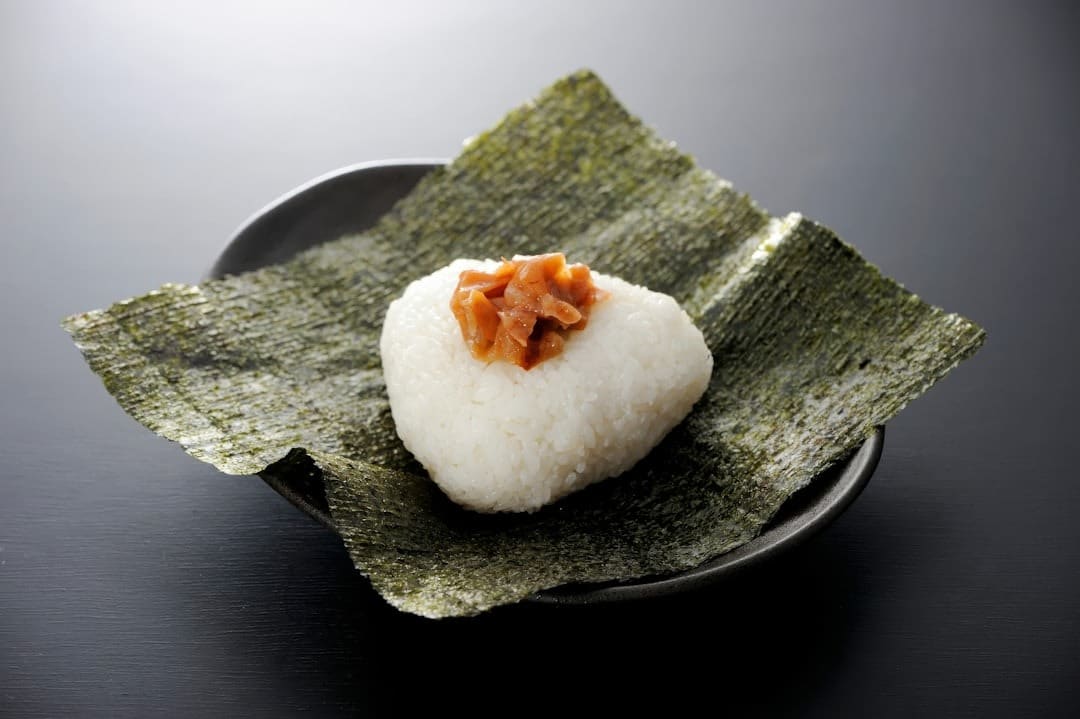 A triangular rice ball topped with pickled ingredients on nori.