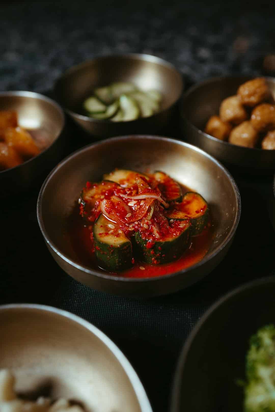 Spicy cucumber kimchi sits in a brass bowl among Korean side dishes.