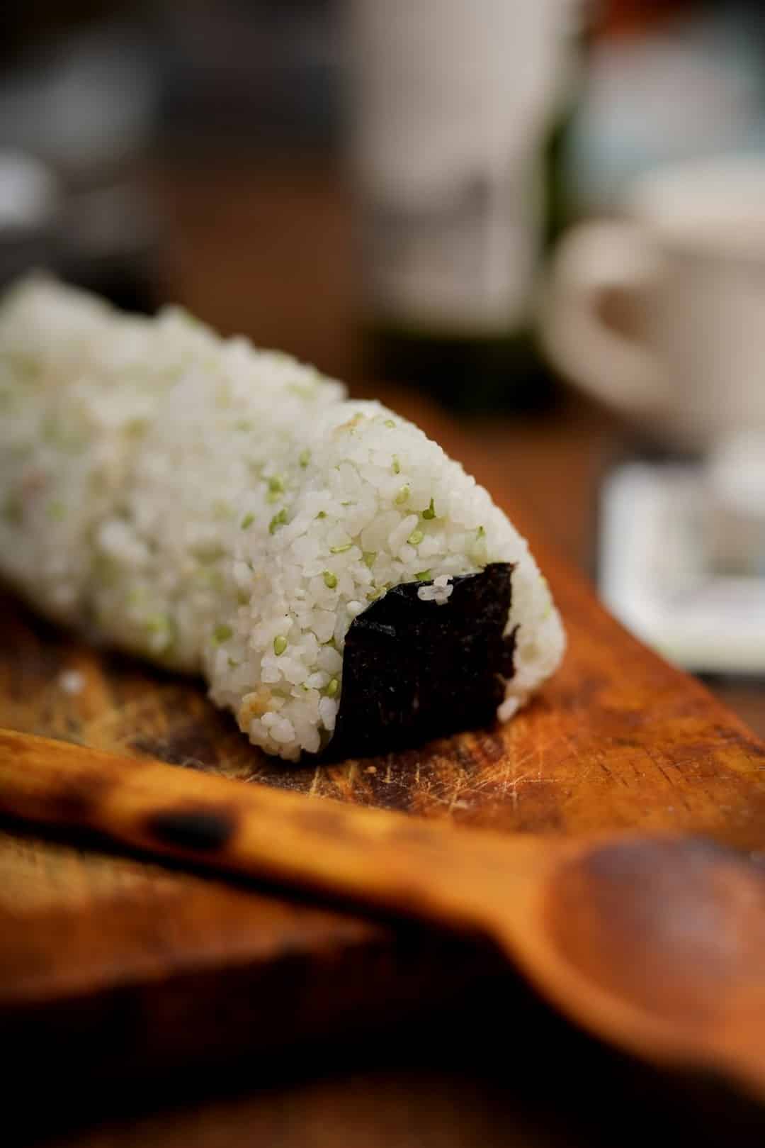 A seaweed wrapped rice ball resting on a wooden board.